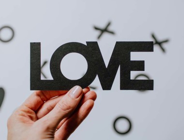 A hand holding up the word 'LOVE' cut out of paper.