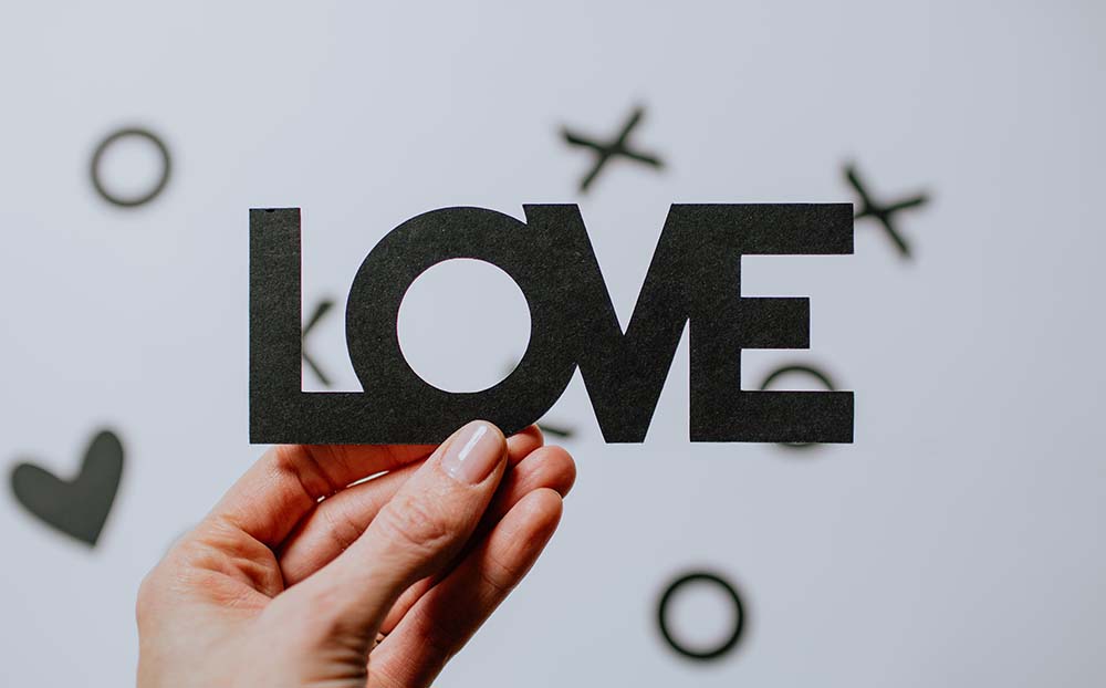 A hand holding up the word 'LOVE' cut out of paper.